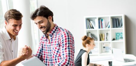 two men congratulating each other while two women sit at a nearby table paperless